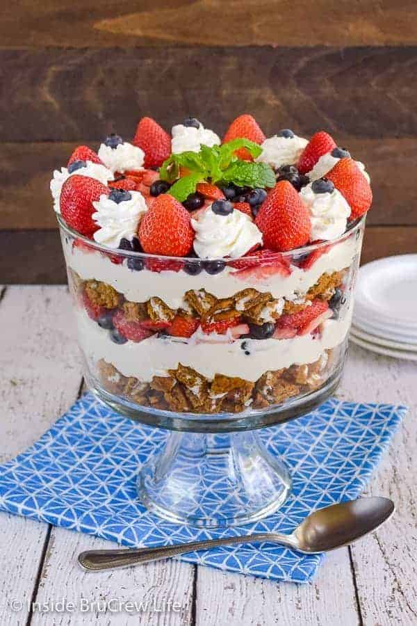A large trifle dish filled with a berry trifle that has layers of snack cakes, no bake cheesecake, and fresh fruit