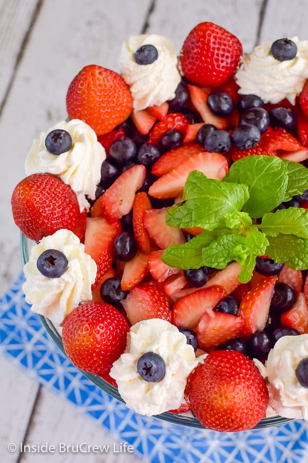 A close up of the top of a berry trifle with strawberries, blueberries, Cool Whip, and mint leaves