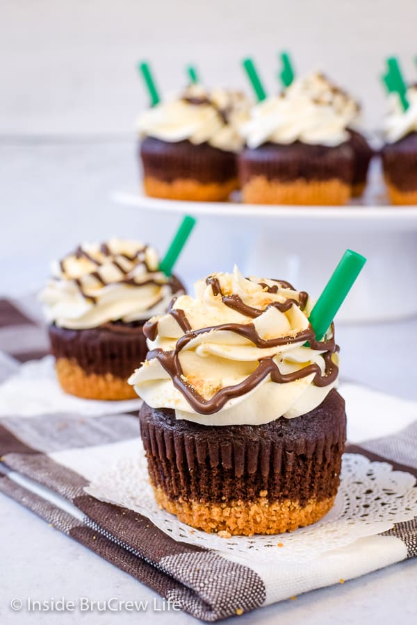 Two chocolate cupcakes topped with marshmallow buttercream and a green straw.