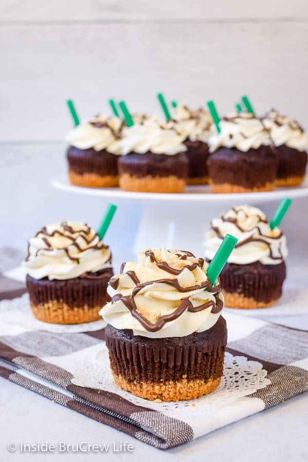 Three chocolate cupcakes topped with marshmallow frosting on a brown and white towel.