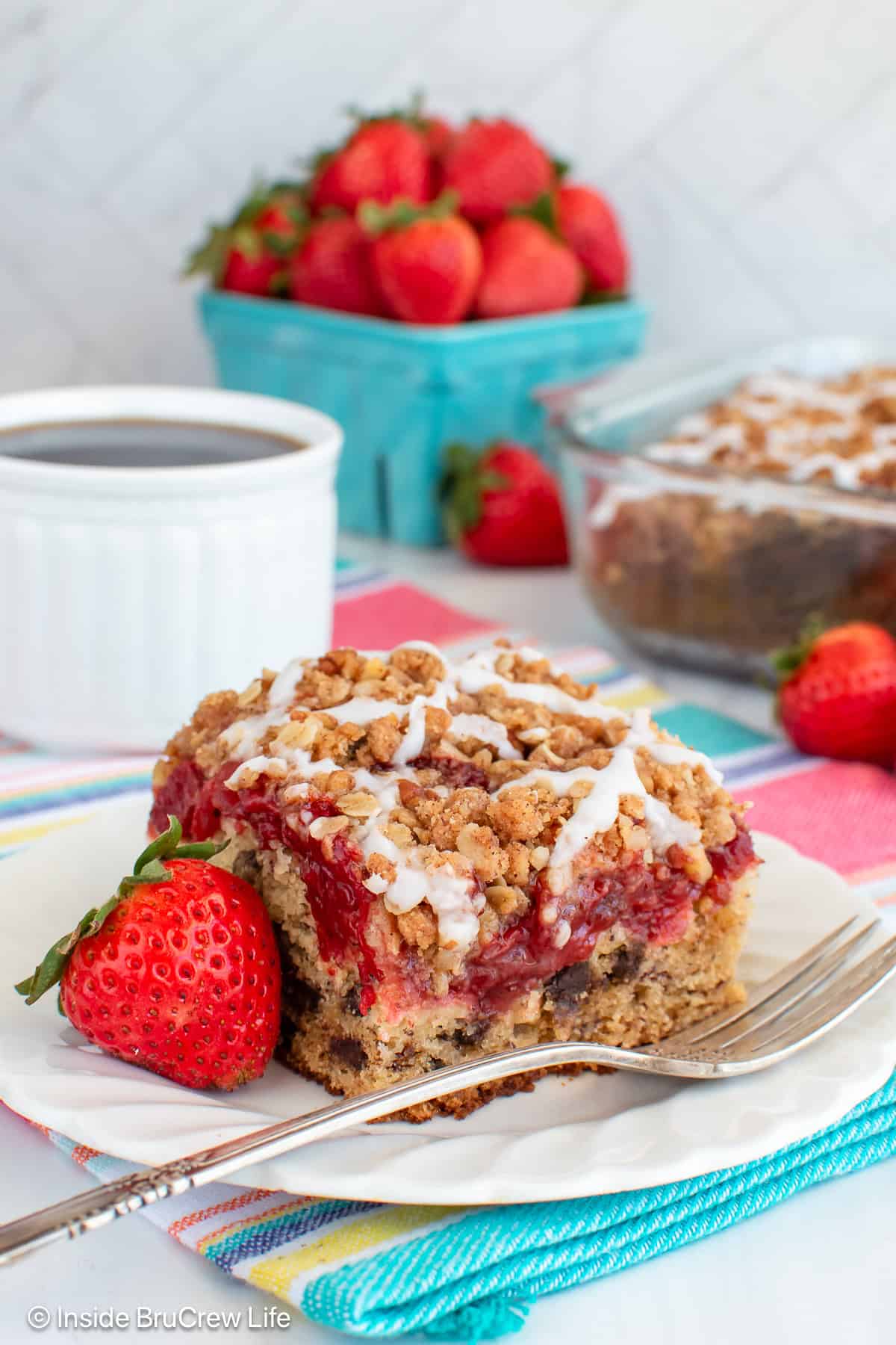 A slice of strawberry banana cake on a white plate and a cup of coffee.