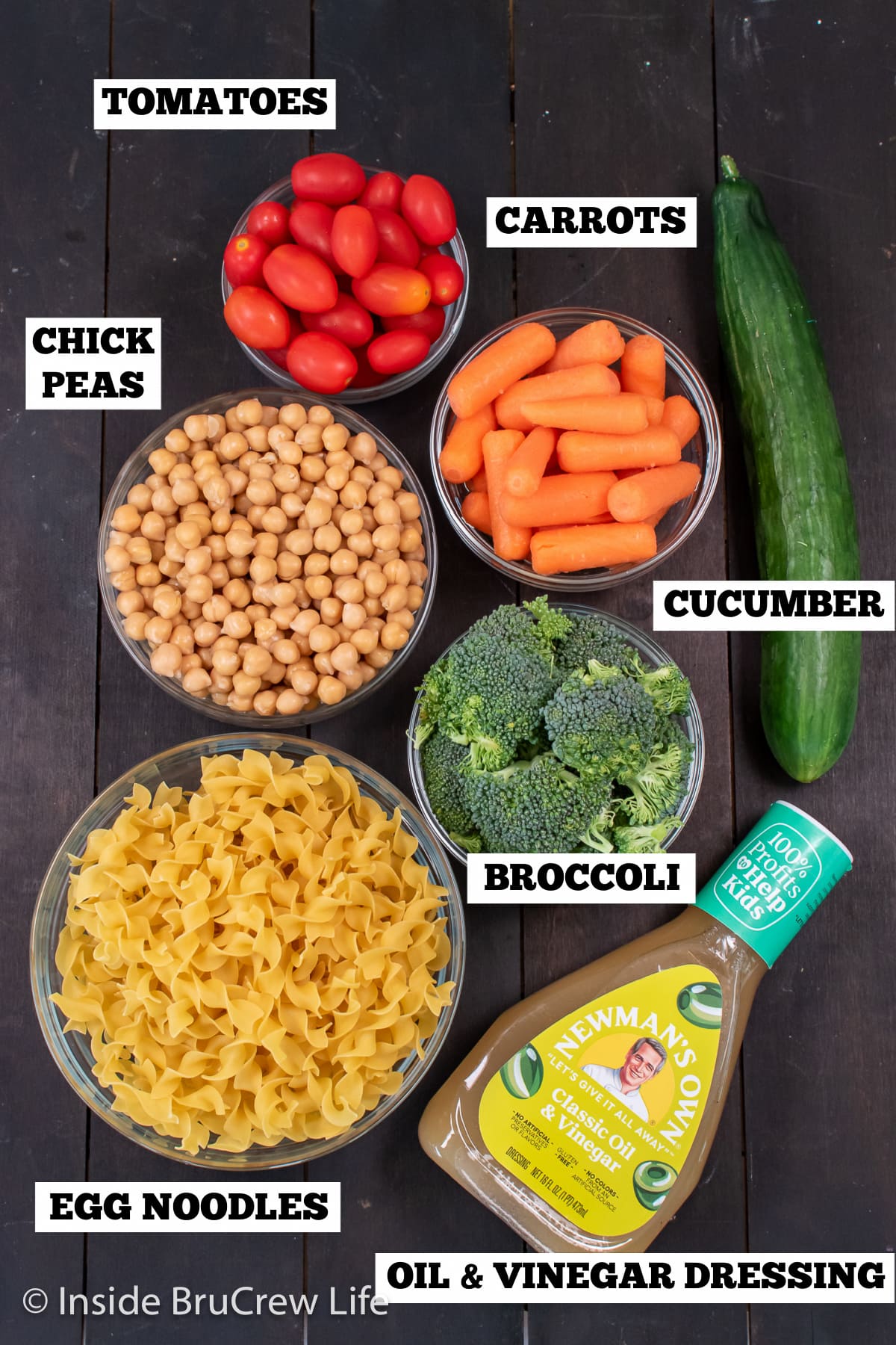 A dark board with bowls of ingredients needed for pasta salad.