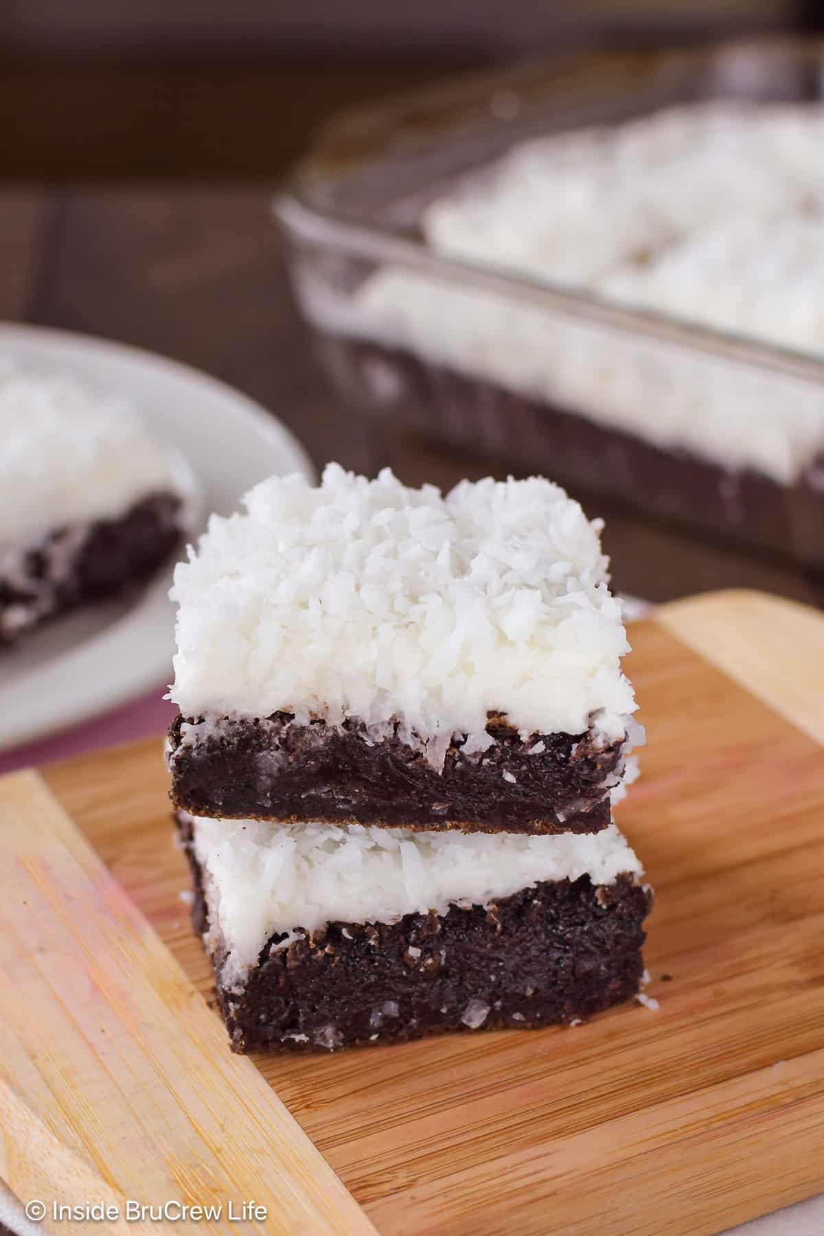 Two brownies topped with coconut frosting on a wooden board.