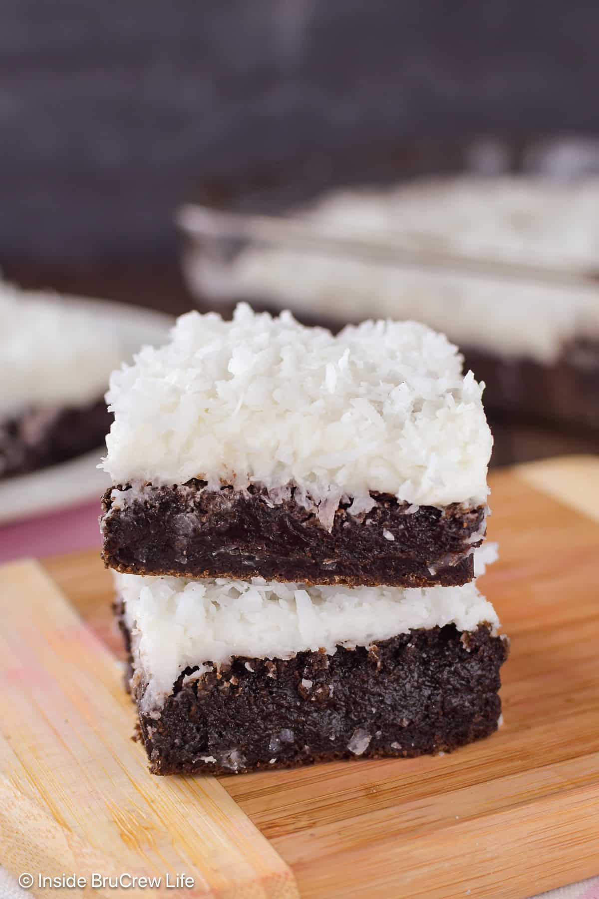 Two coconut oil brownies with frosting stacked on a wooden board.