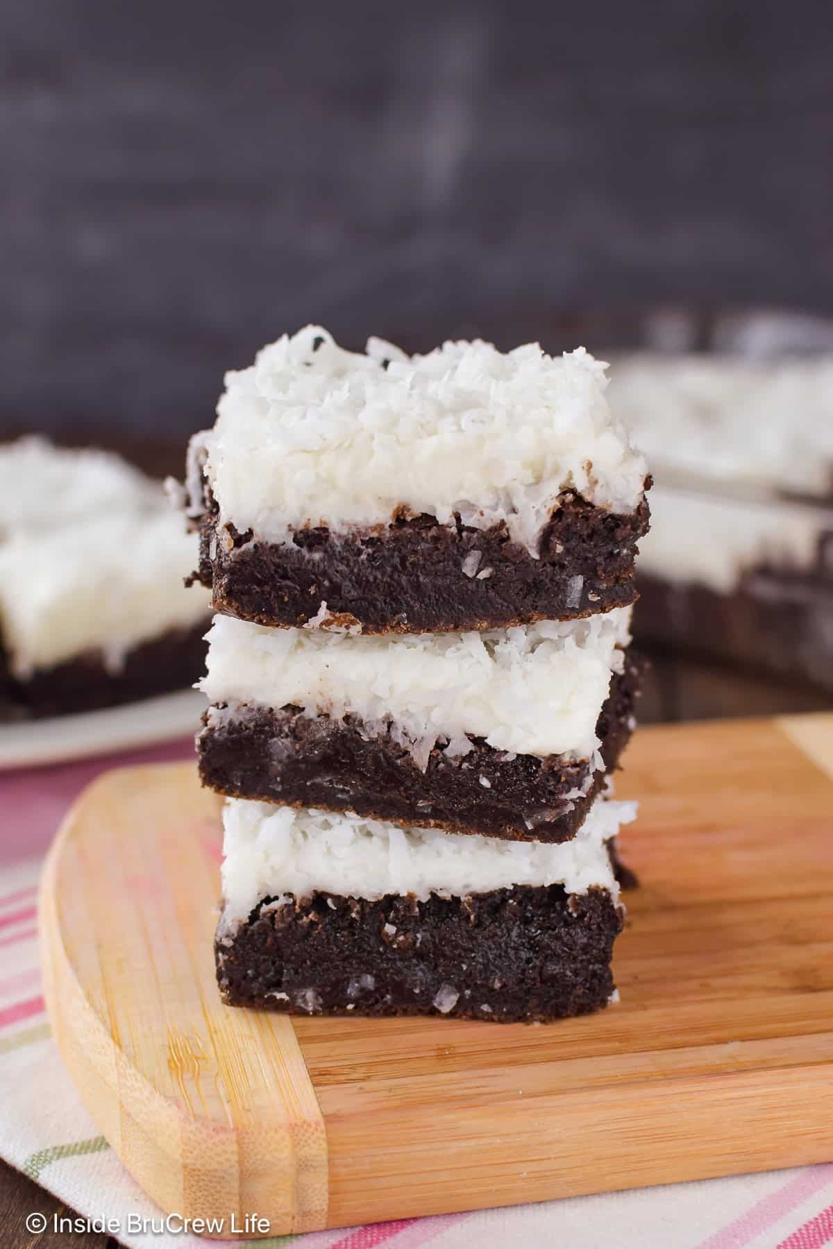 A stack of three frosted coconut brownies on a wooden board.