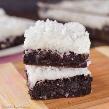 Two coconut oil brownies with frosting stacked on a wooden board.