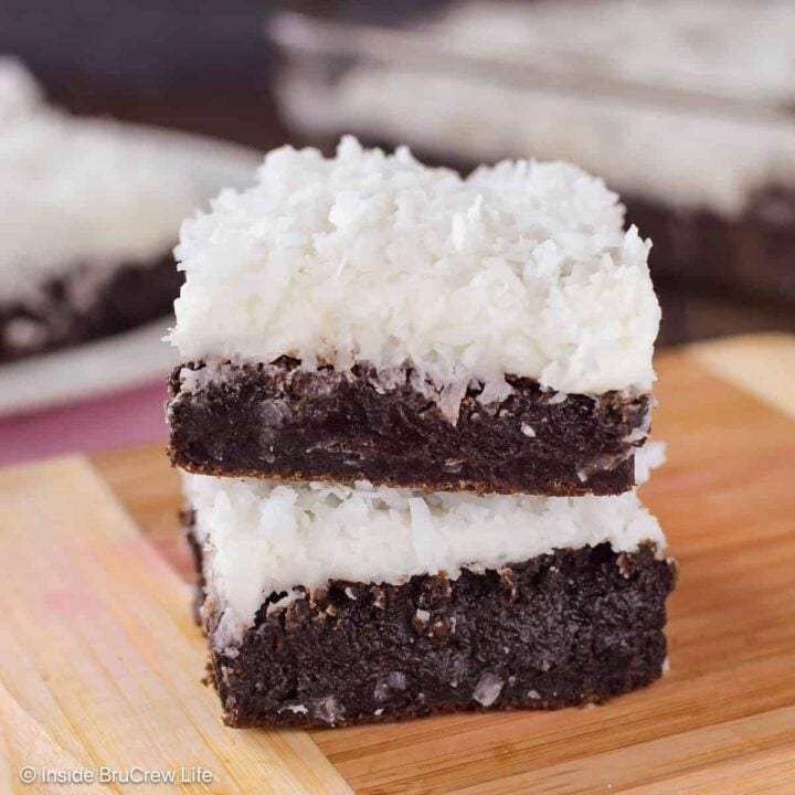 Two coconut oil brownies with frosting stacked on a wooden board.