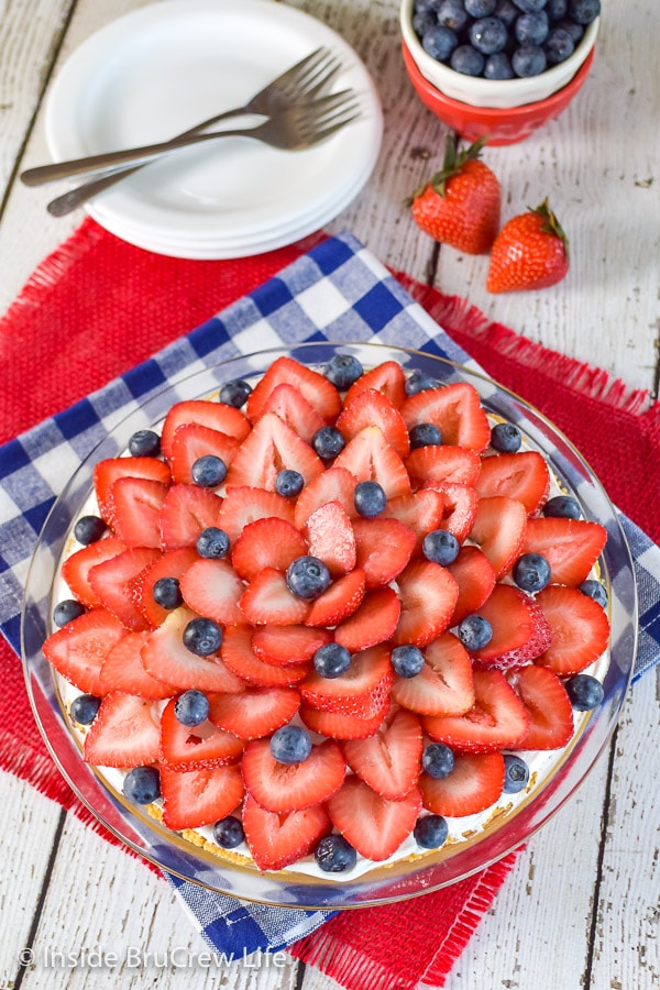 An above picture of the top of a strawberry lemon cream pie on a blue and white checkered towel