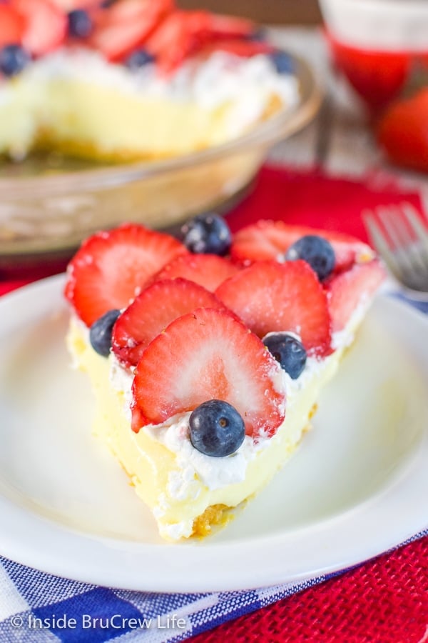 A white plate with a slice of strawberry lemon cream pie on it and more pie behind it