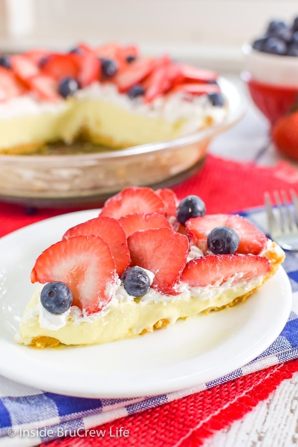 A white plate with a slice of no bake strawberry lemon cream pie and more pie behind it