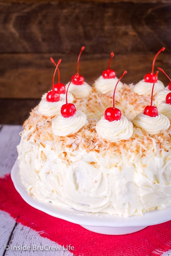 A picture of the side of a pina colada bundt cake decorated with frosting, coconut, and cherries