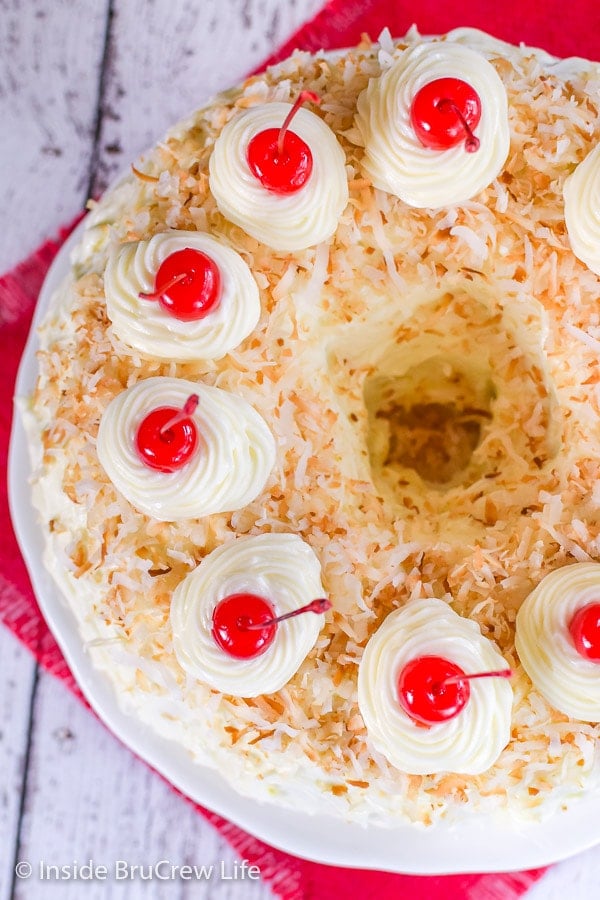 An overhead picture of the top of a pina colada bundt cake topped with frosting, toasted coconut, and cherries