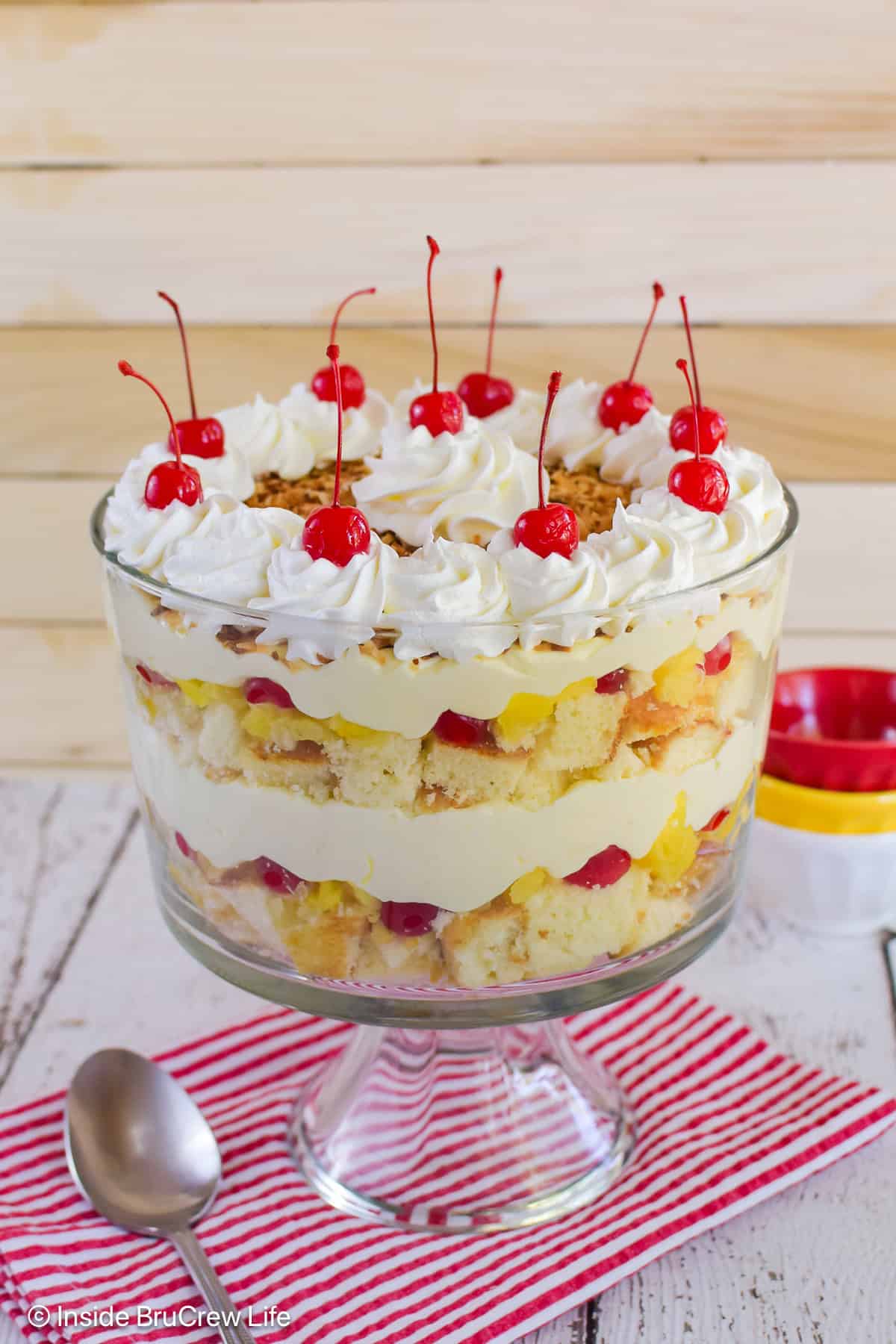 A large clear bowl filled with a pina colada trifle and topped with cherries.
