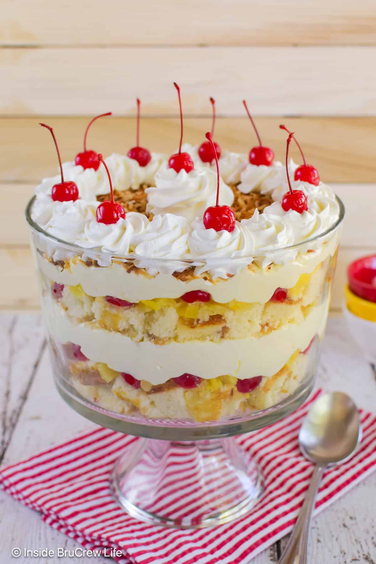 A large clear bowl filled with a pina colada trifle and topped with cherries.
