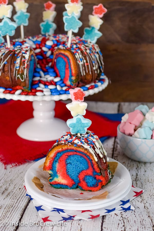 A white plate with a slice of red white and blue bundt cake with a marshmallow pop in the top and the cake behind it