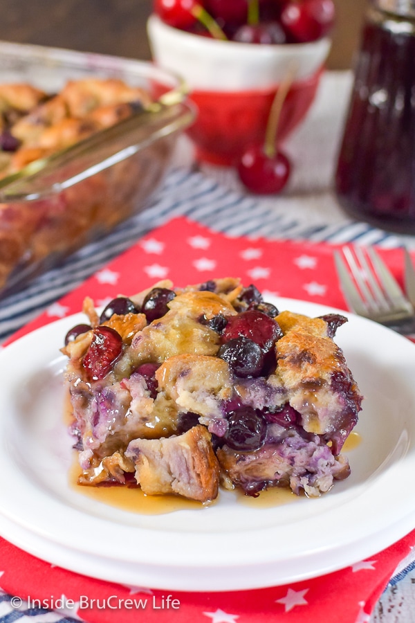 A white plate on a red towel with a square of cherry blueberry french toast bake on it