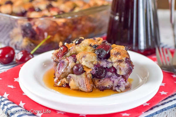 Two white plates stacked together with cherry blueberry french toast bake on it in a puddle of syrup