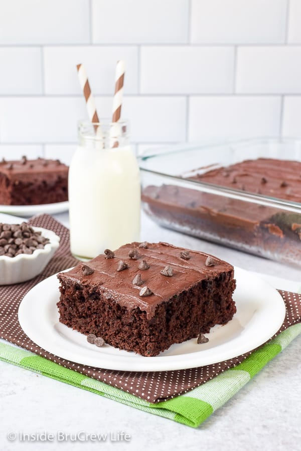 A white plate with a slice of chocolate zucchini brownies topped with chocolate frosting.