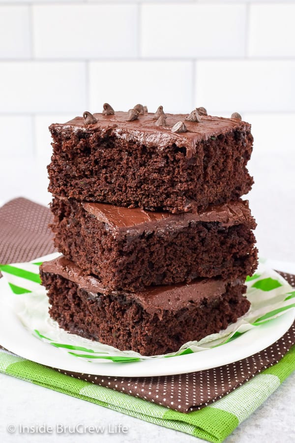 A white plate with three frosted zucchini brownies stacked on it.