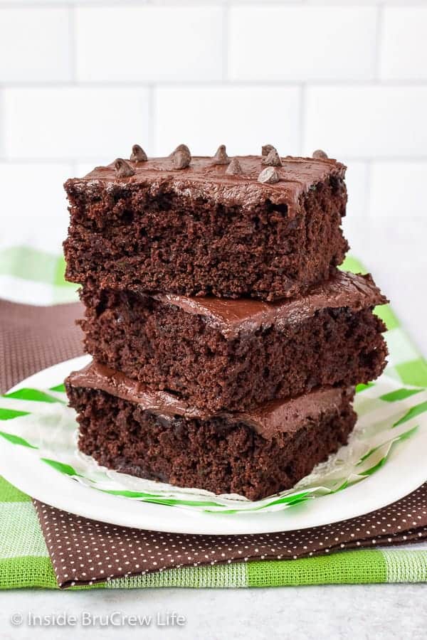 A white plate with three frosted zucchini brownies stacked on it.