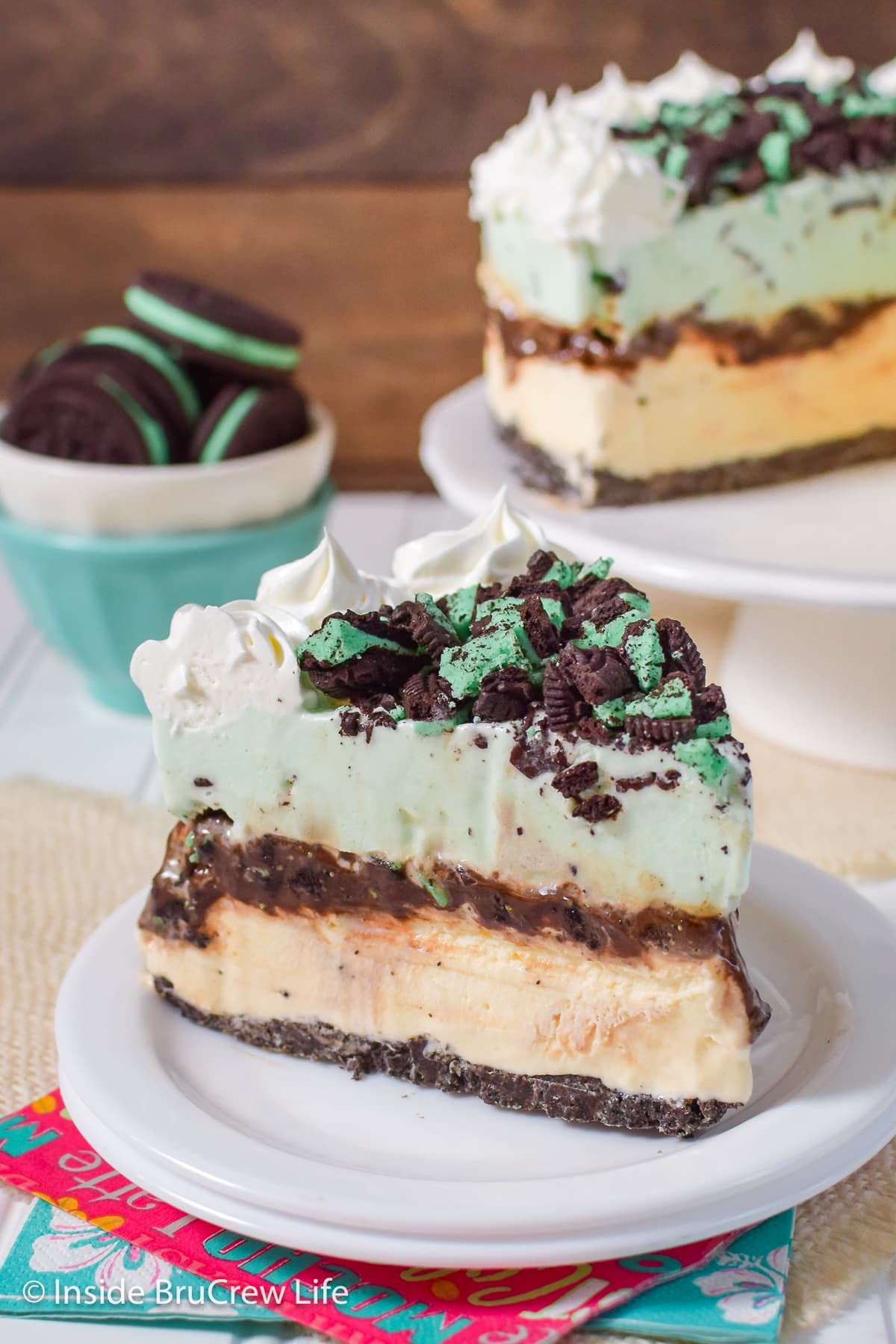 A slice of ice cream cake topped with Oreo cookies and Cool Whip on a white plate.