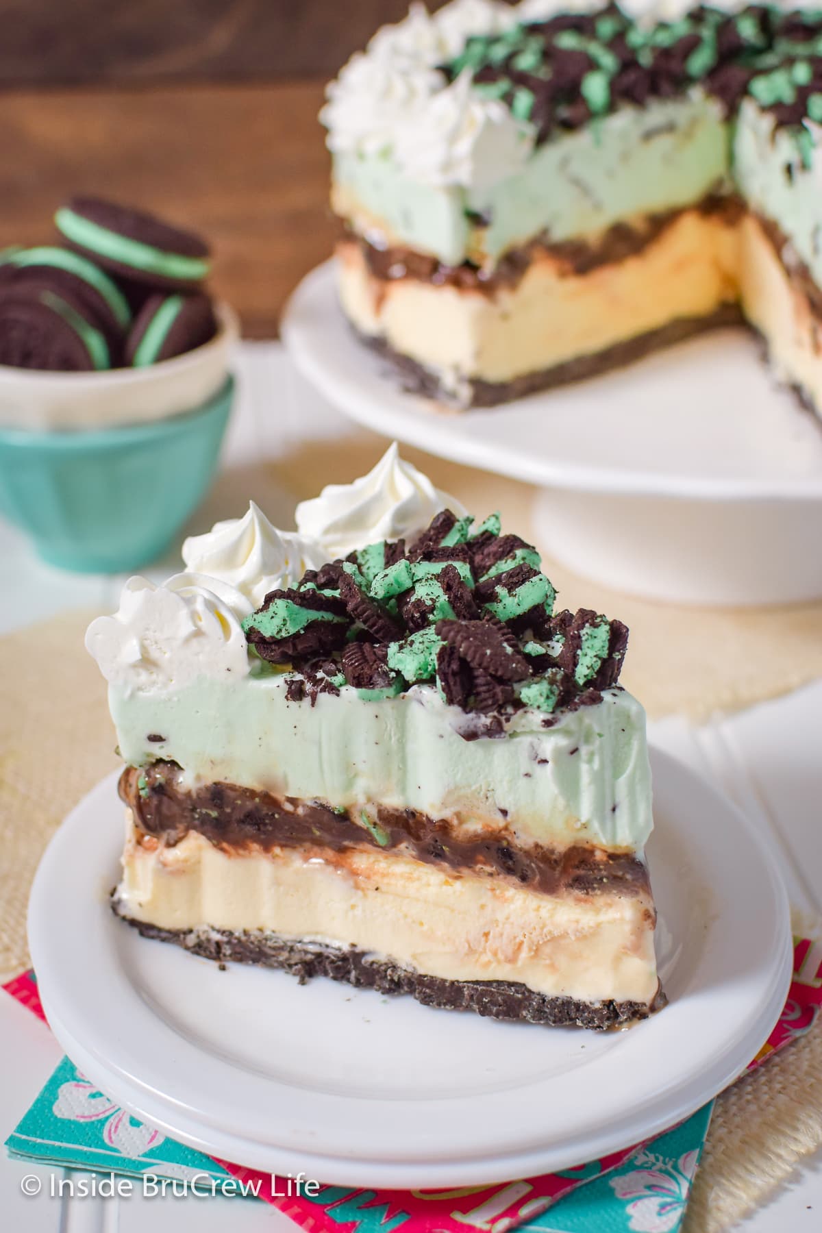 A slice of ice cream cake topped with Oreo cookies and Cool Whip on a white plate.