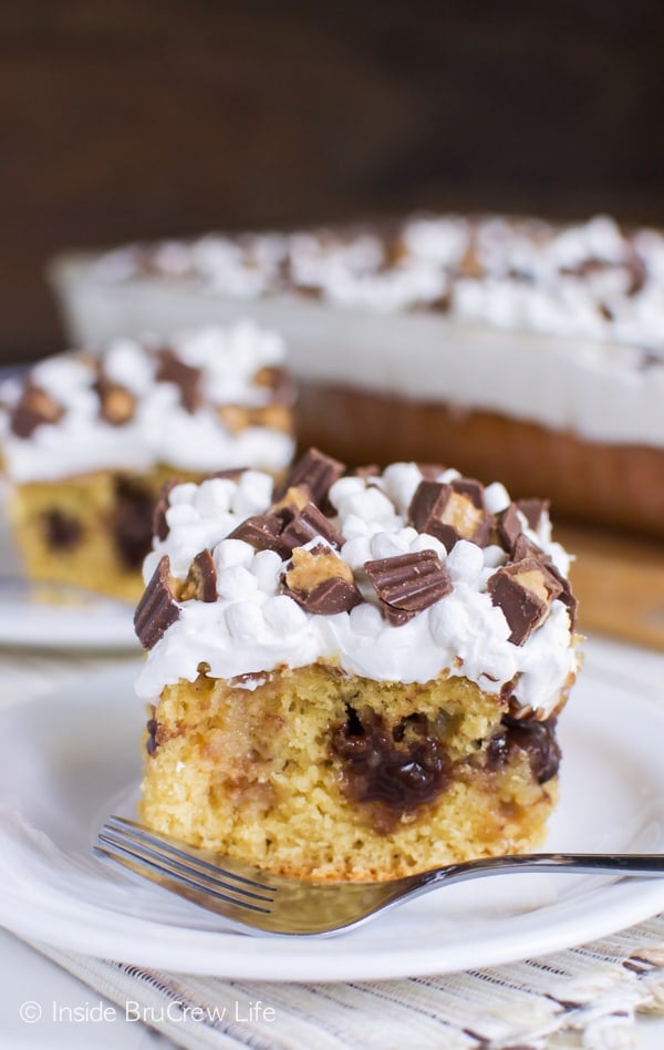 Two white plates with a square of peanut butter fudge poke cake on each one and a cake in the background