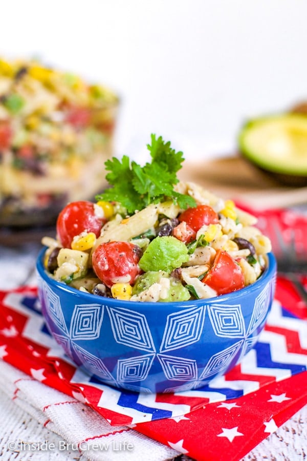 A red towel with a blue bowl filled with a creamy pasta salad loaded with veggies in it