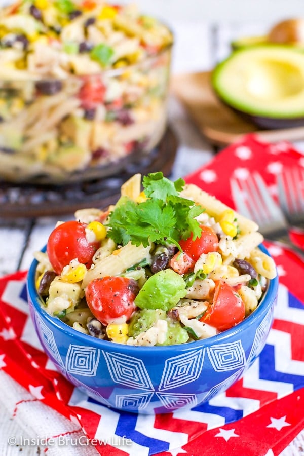 A blue bowl on a red towel filled with a ranch pasta salad that is loaded with veggies and chicken