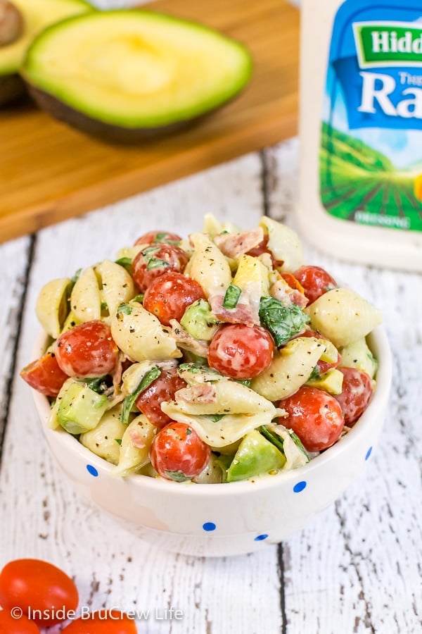 A white bowl filled with a creamy ranch BLT pasta salad and cut avocados behind it