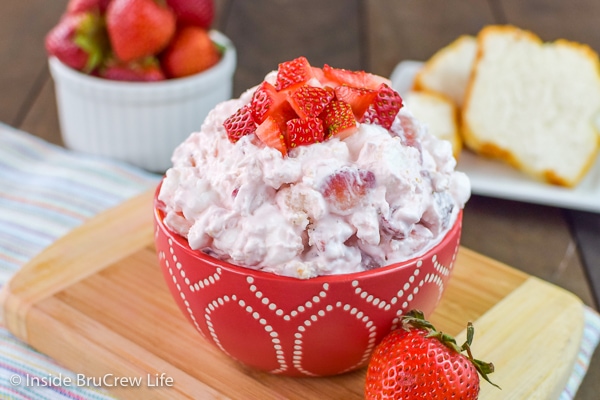 A red bowl on a cutting board filled with strawberry fluff salad and topped with diced strawberries