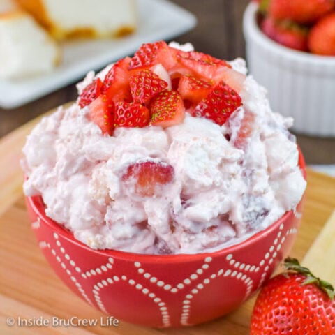 A red bowl full of strawberry fluff salad and topped with diced strawberries
