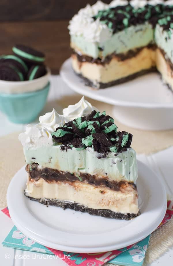 A white plate with a slice of ice cream cake topped with mint oreos and whipped cream