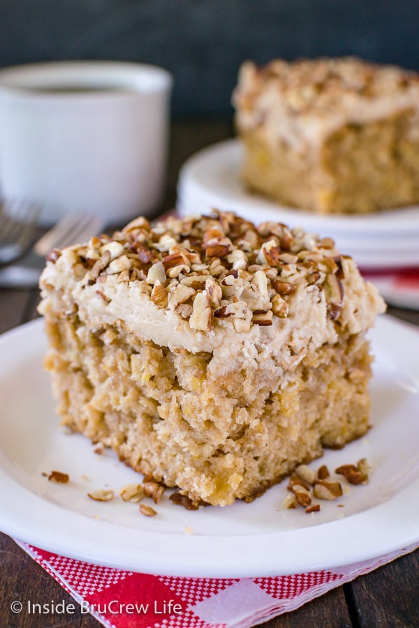 A close up picture of a piece of apple praline cake topped with frosting and pecans on a white plate