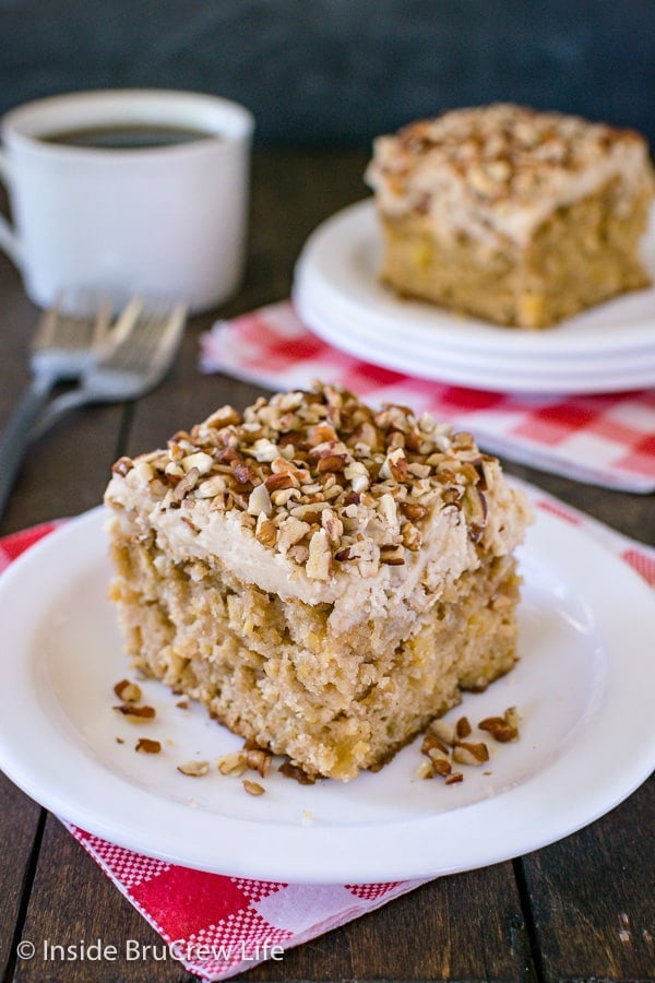 A white plate with a square of apple praline cake on it and a coffee cup behind it