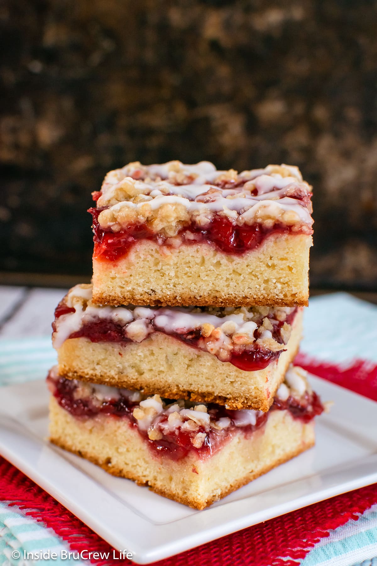 A stack of three squares of coffee cake made with cherries on a white plate.
