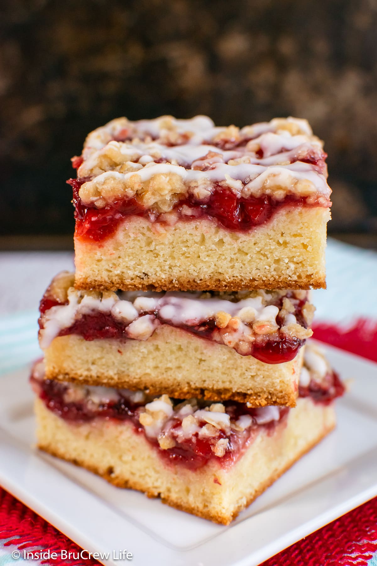 A stack of three squares of coffee cake made with cherries on a white plate.