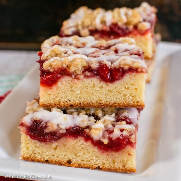 Squares of coffee cake with cherries on a white plate.