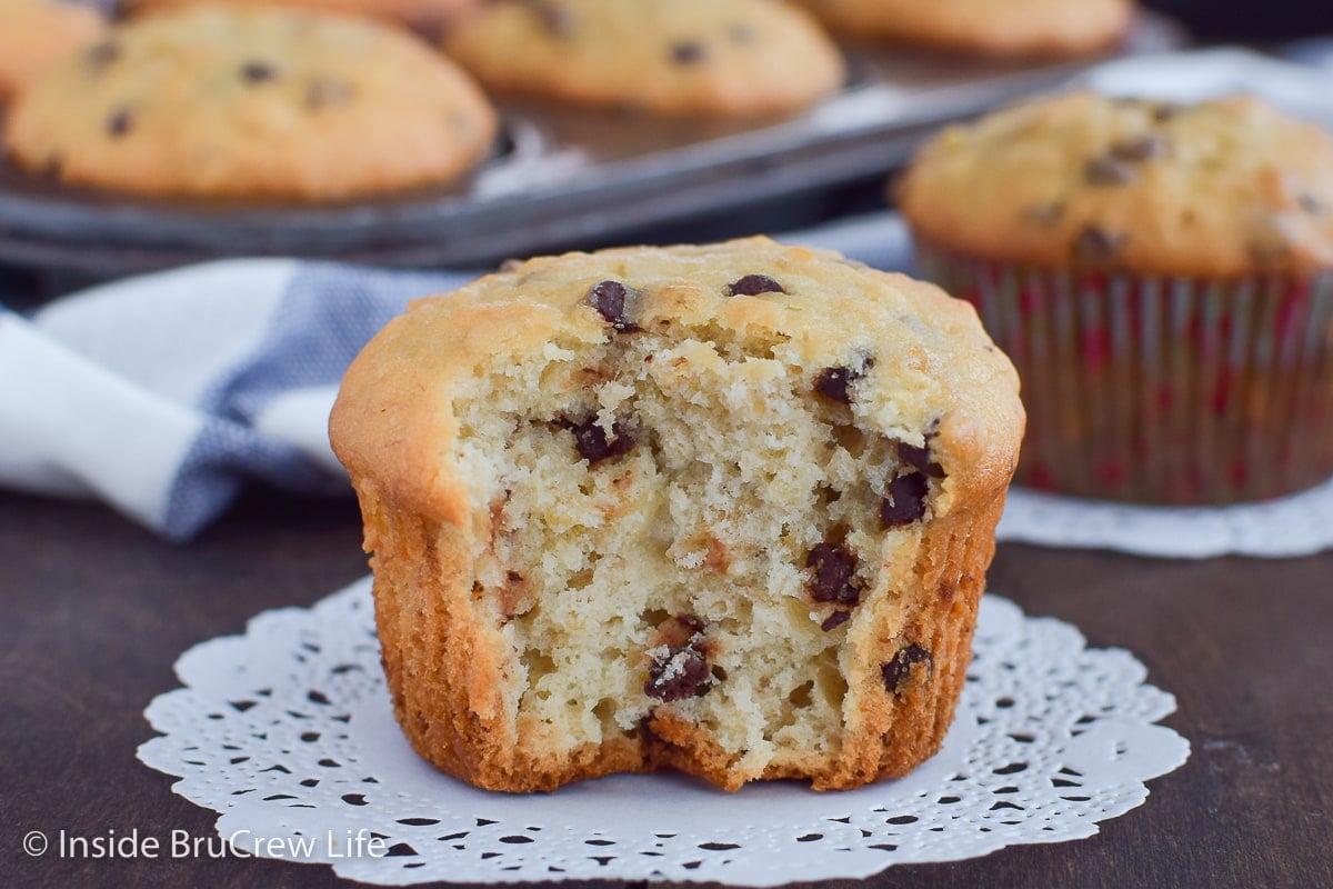 A fluffy banana muffin with a bite out of the front on white paper.