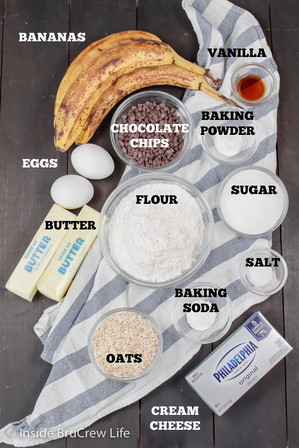 A brown board with bowls of ingredients needed to make banana muffins.