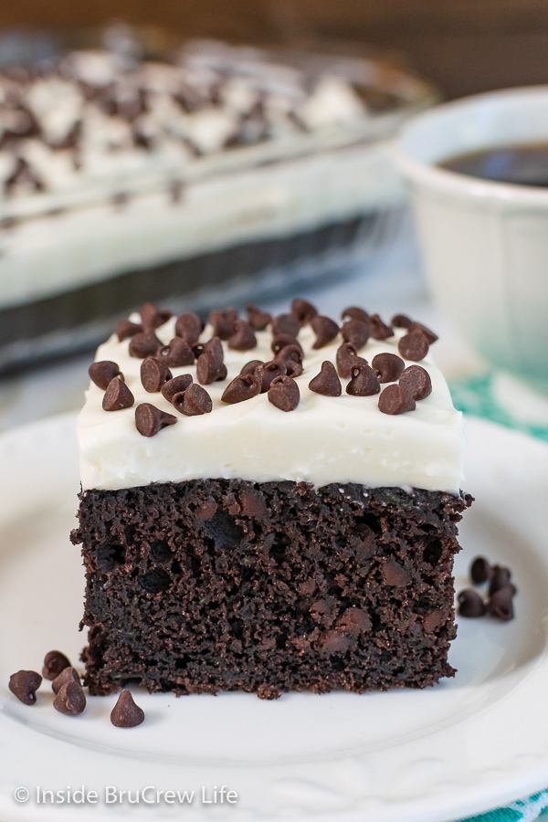 A square of chocolate chip zucchini cake with frosting on a white plate.