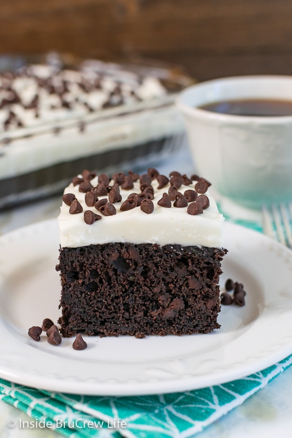 A square of chocolate zucchini cake with frosting on a white plate.