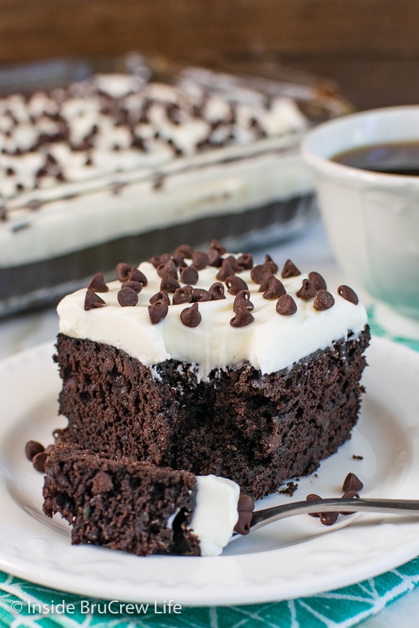 A white plate with a slice of frosted chocolate chip zucchini cake with a bite take out of it.