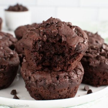 Chocolate zucchini muffins stacked on a plate with a bite out of the top one.
