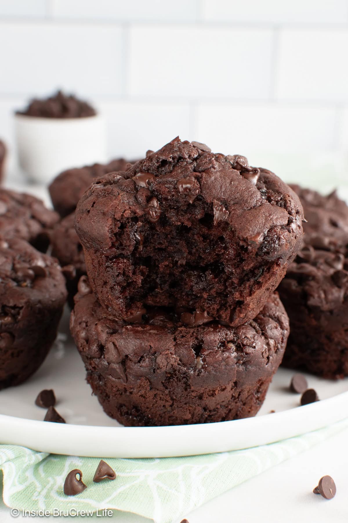 Chocolate zucchini muffins stacked on a plate with a bite out of the top one.