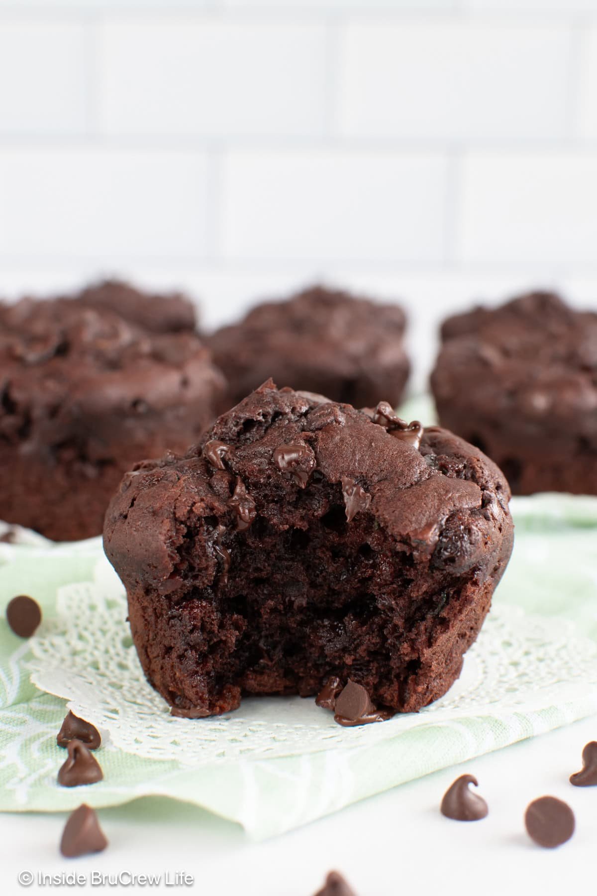 Chocolate chocolate chip zucchini muffins on a white board with a bite out of one.