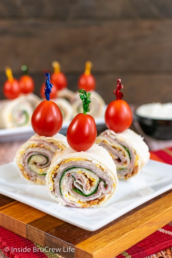 Three turkey club pinwheels topped with cherry tomatoes on a white plate