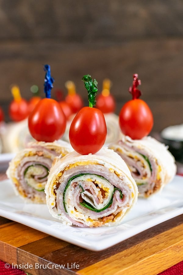 A white plate with three turkey club pinwheels standing up with a toothpick and cherry tomato