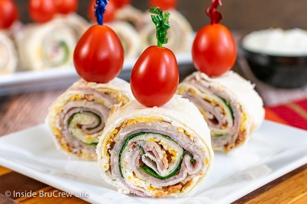 Three turkey club pinwheels on a white plate topped with a toothpick and cherry tomato