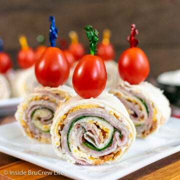 Three turkey club pinwheels on a white plate topped with tomatoes